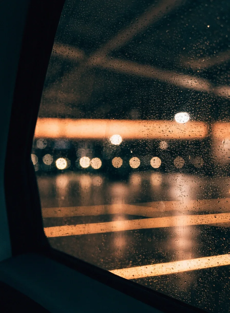 Rain on a car window at night with warm car-park bay lights behind it
